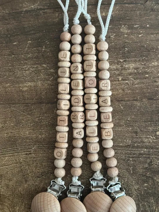 "Wooden bead lanyard with letter beads spelling out a name on a wooden surface"