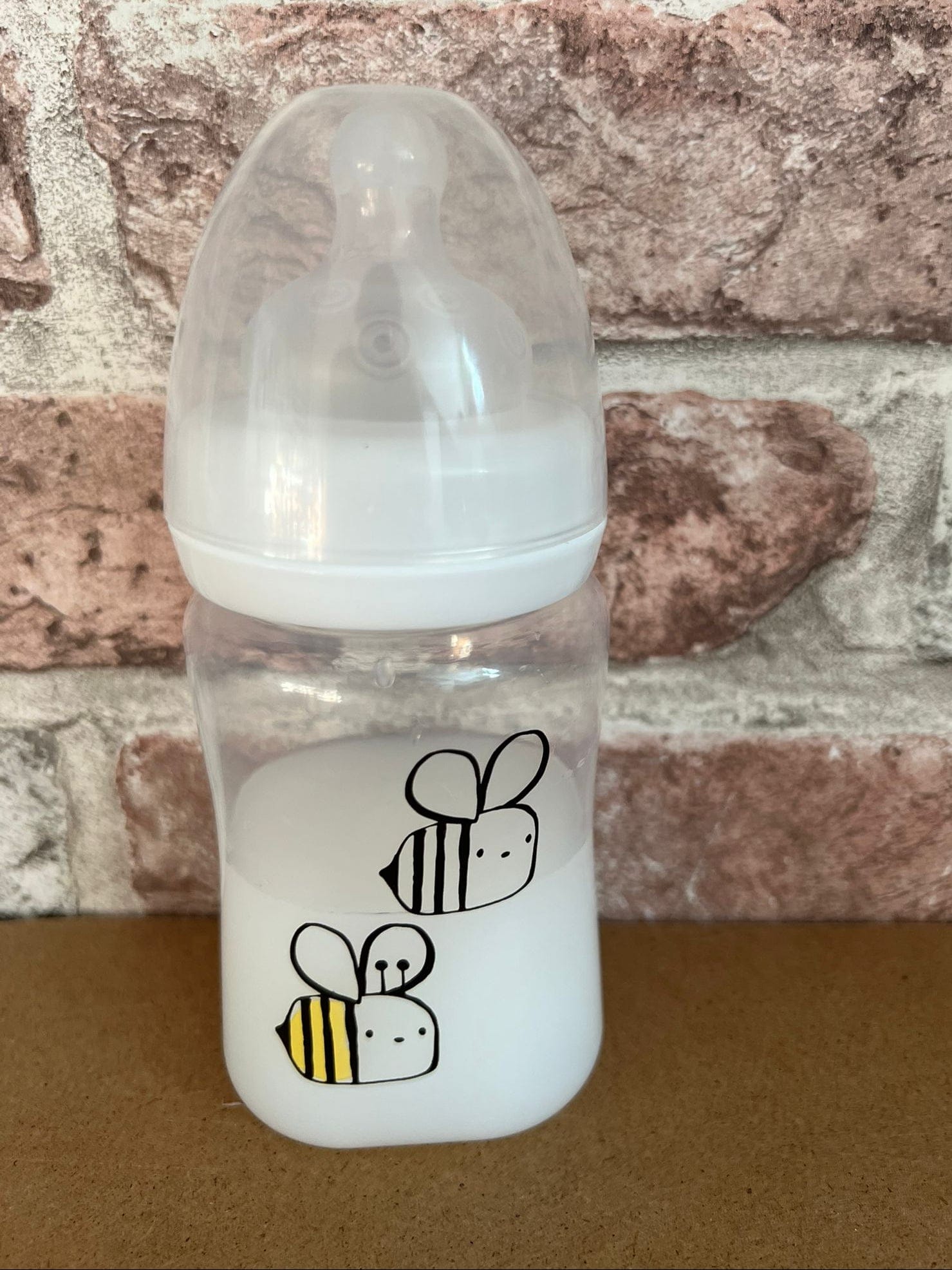 "Clear baby bottle with bee designs on a brick wall background willow tree reborns UK"