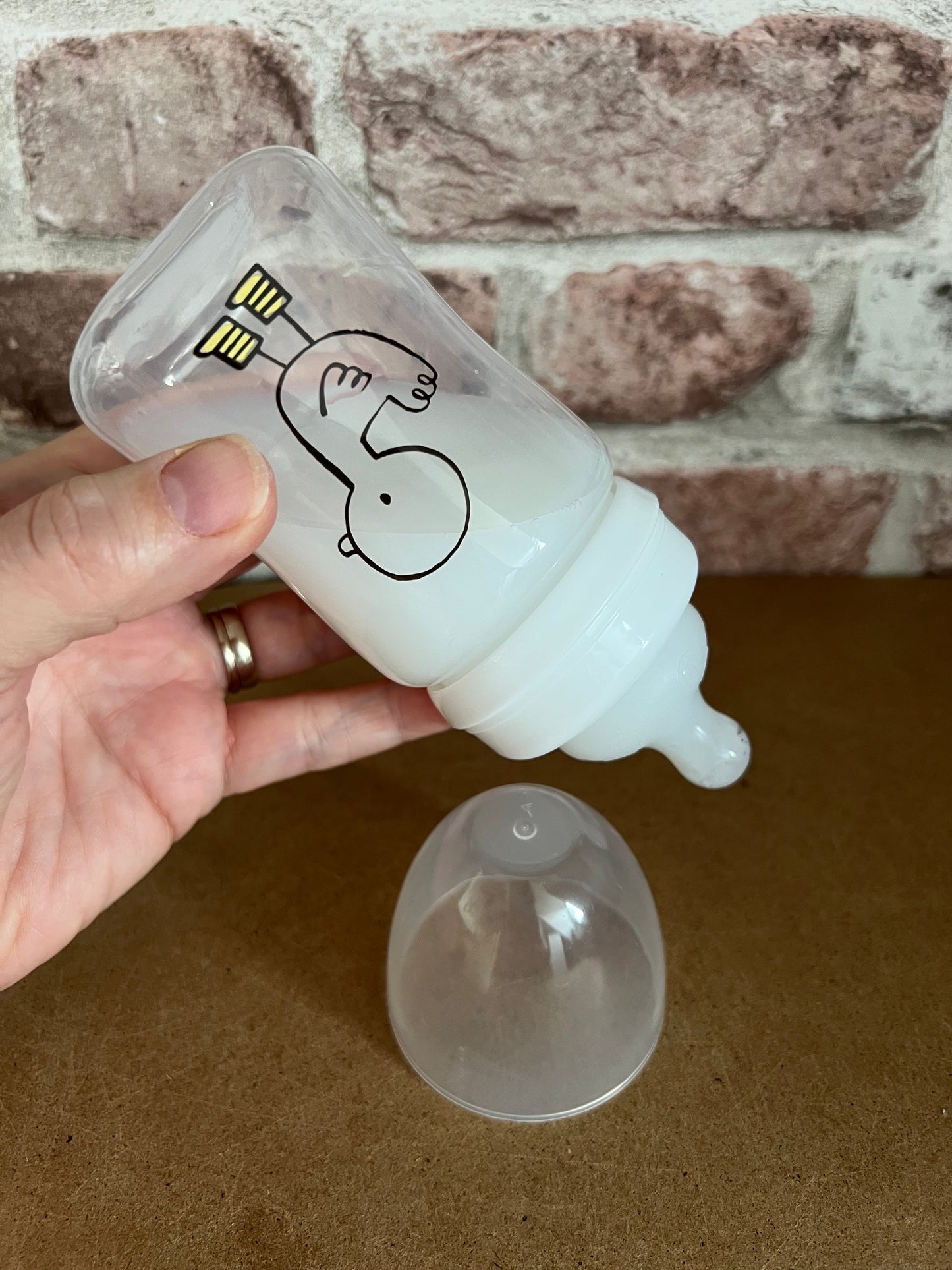 Hand holding a white baby bottle with a cartoon design against a stone wall background willow tree reborns UK