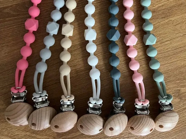 Set of colorful pacifier clips with wooden ends on a wooden surface