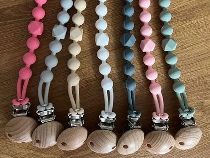 Set of colorful pacifier clips with wooden ends on a wooden surface